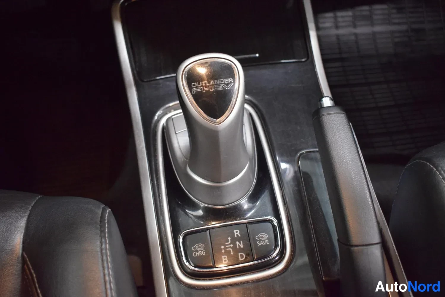 Yksityiskohta: Automan-vaihteenvalitsin, jossa lukee Outlander PHEV; pätkkyysnappien kohdalla R, N, D, B sekä CHRG- ja SAVE-painikkeet.