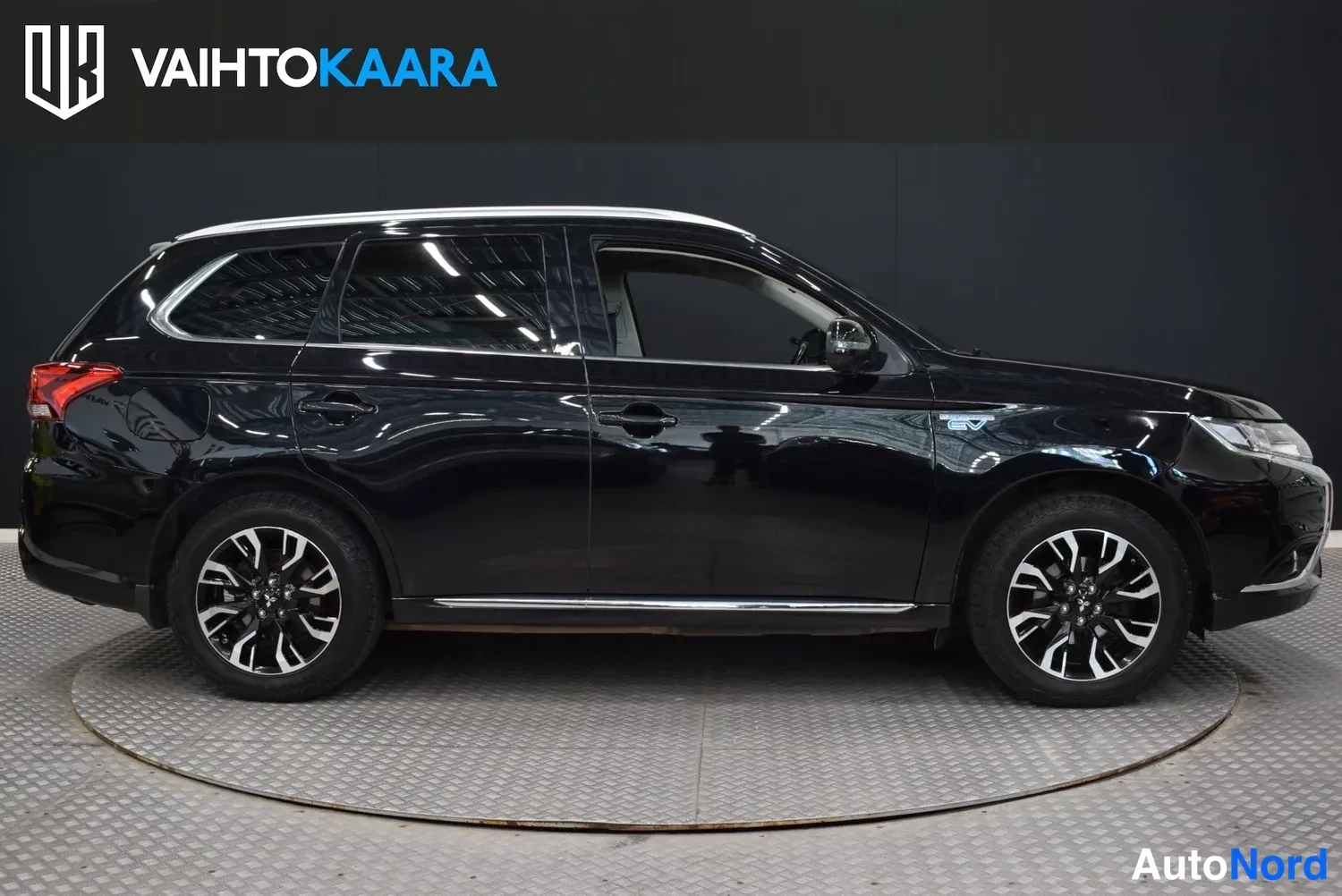 Sivulta: Musta Mitsubishi Outlander sivulta oikealta katsottuna studiotaustaa vasten, katossa kattokaiteet ja 18 tuuman kevytmetallivanteet.