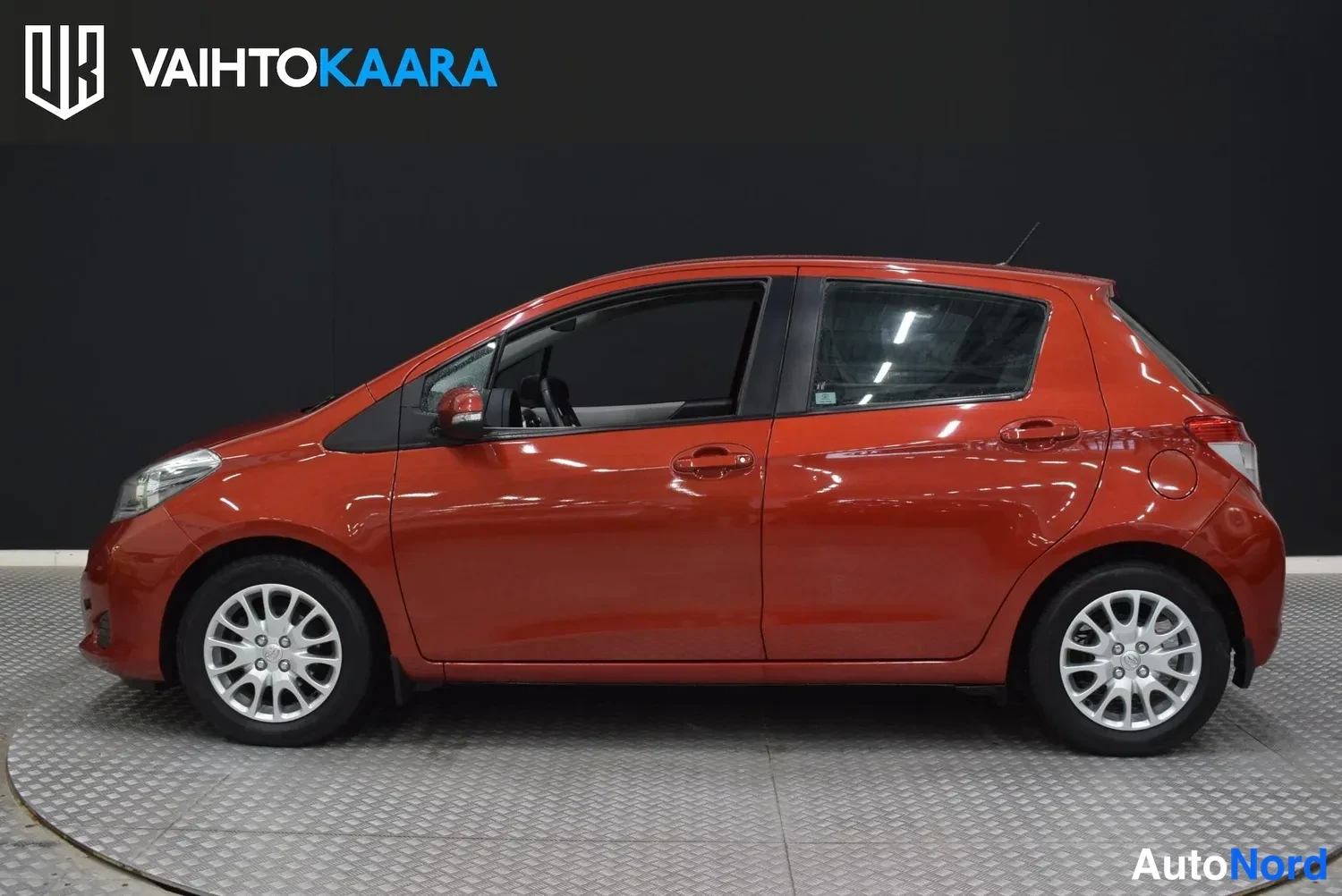Sivulta: Toyota Yaris -viistoperän vasen sivuprofiili, punainen kori ja hopeiset kevytmetallivanteet.
