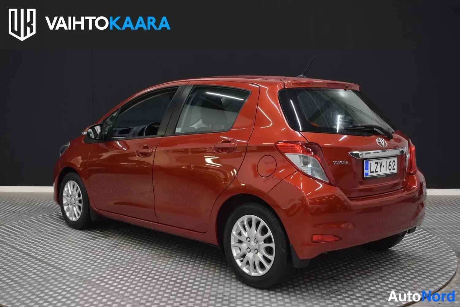Takaviisto: Toyota Yaris takaviistosta vasemmalle suunnattuna, punainen kori, takavalo ja rekisterikilpi näkyvissä.