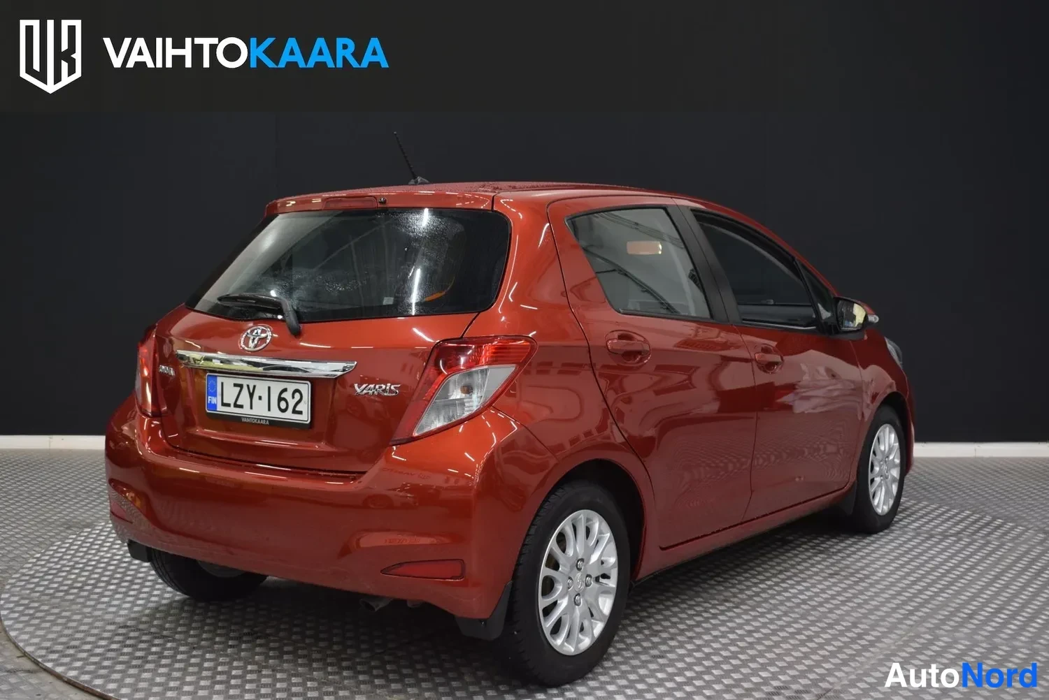 Takaviisto: Toyota Yaris takaviistosta oikealle suunnattuna, punainen kori, takaluukun VARIKS-teksti ja rekisterikilpi näkyvissä.