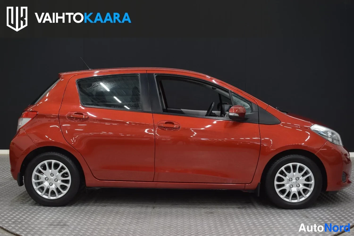 Sivulta: Punaisen Toyota Yaris -henkilöauton sivukuva oikealta sivulta, neljästä ovesta ja kevytmetallivanteista.