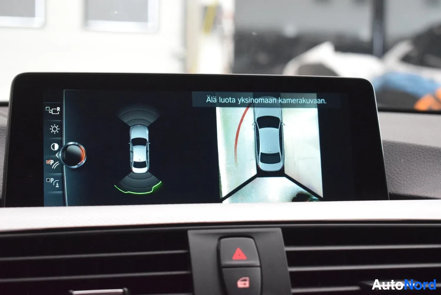 Muu: Auton infotainment-näyttö näyttää kamera- ja tutkakuvan parkkeerauksen tueksi tekstillä 'Älä luota yksinomaan kamerakuvaan.'
