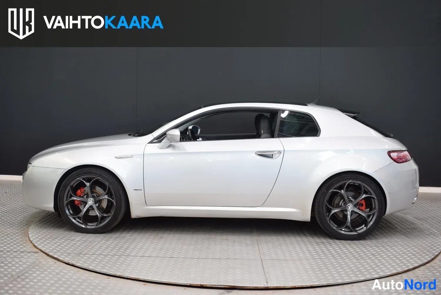 Sivulta: Hopeanharmaa Alfa Romeo Brera kyljestä vasemmalta kuvattuna studiossa; tummat kevytmetallivanteet ja punaiset jarrusatulat näkyvät.