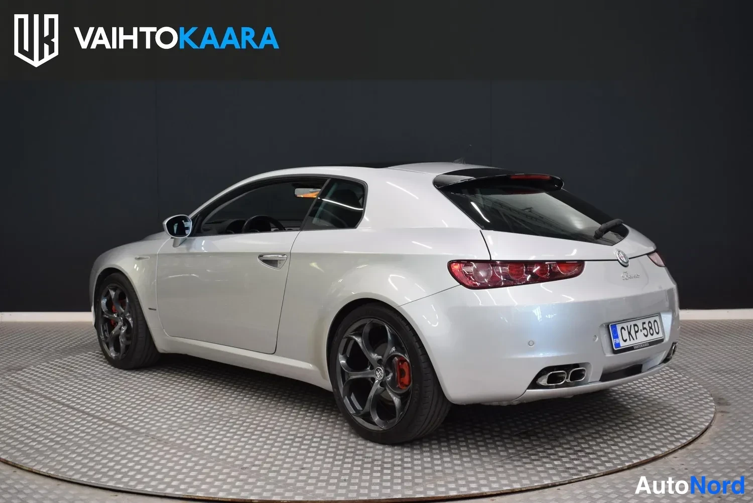 Takaviisto: Hopeanharmaa Alfa Romeo Brera kolmesta neljäsosasta takaa oikealta kuvattuna studiossa; kaksoispakoputket ja rekisteritunnus näkyvät.