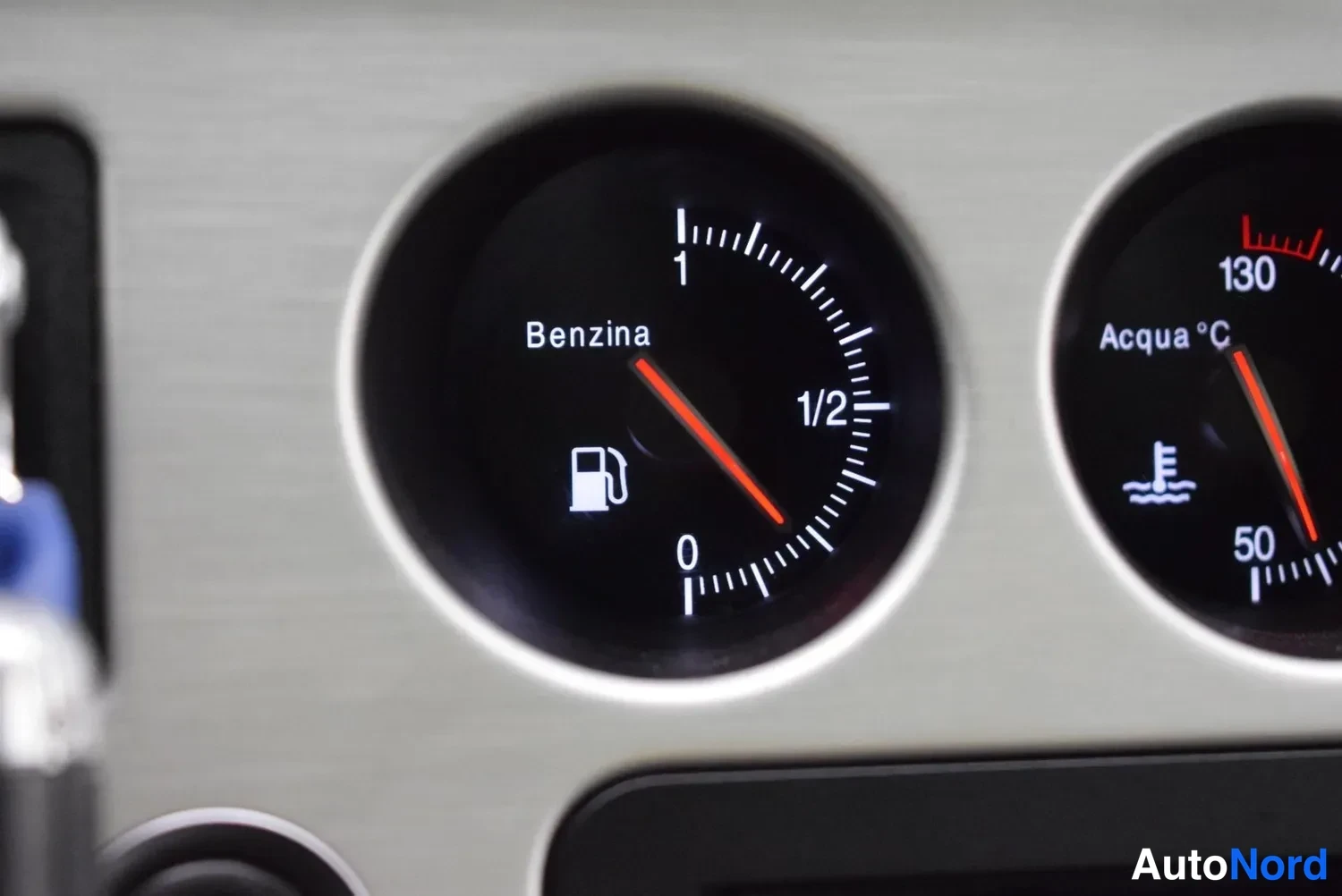 Muu: Mittariston lähikuva: polttoainemittari, jonka asteikko on merkitty Benzina, 0, 1/2 ja 1, neula puolivälin alapuolella; vieressä osittain näkyvä vesilämpömittar