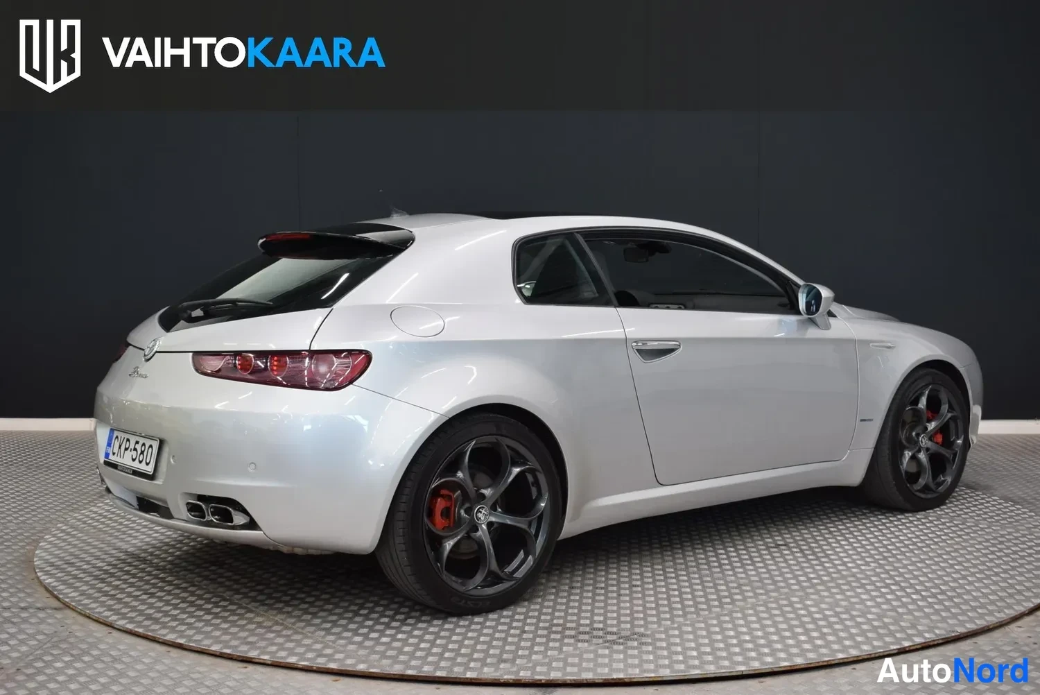Takaviisto: Hopeanharmaa Alfa Romeo Brera kolmesta neljäsosasta takaa vasemmalta kuvattuna studiossa; takavalot ja rekisteritunnus näkyvät.
