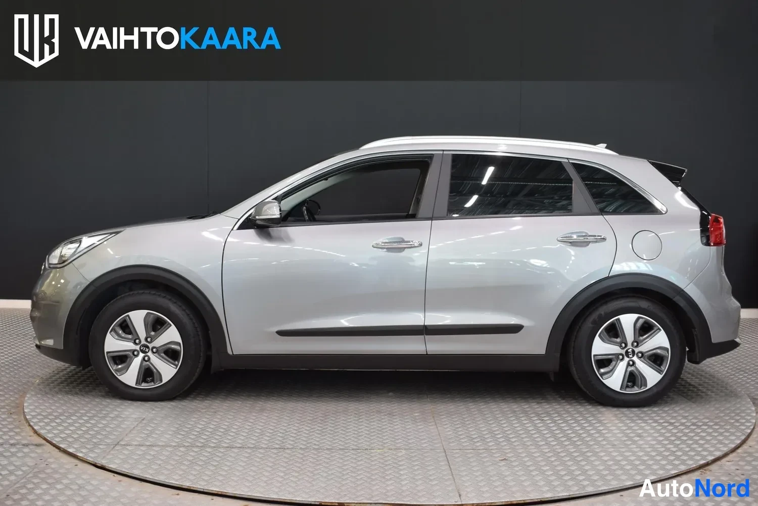 Sivulta: Kia Niro -auton sivuprofiili vasemmalta, hopea koriväri, kattokaiteet ja mustat muovilistat ovien alapuolella näkyvät.
