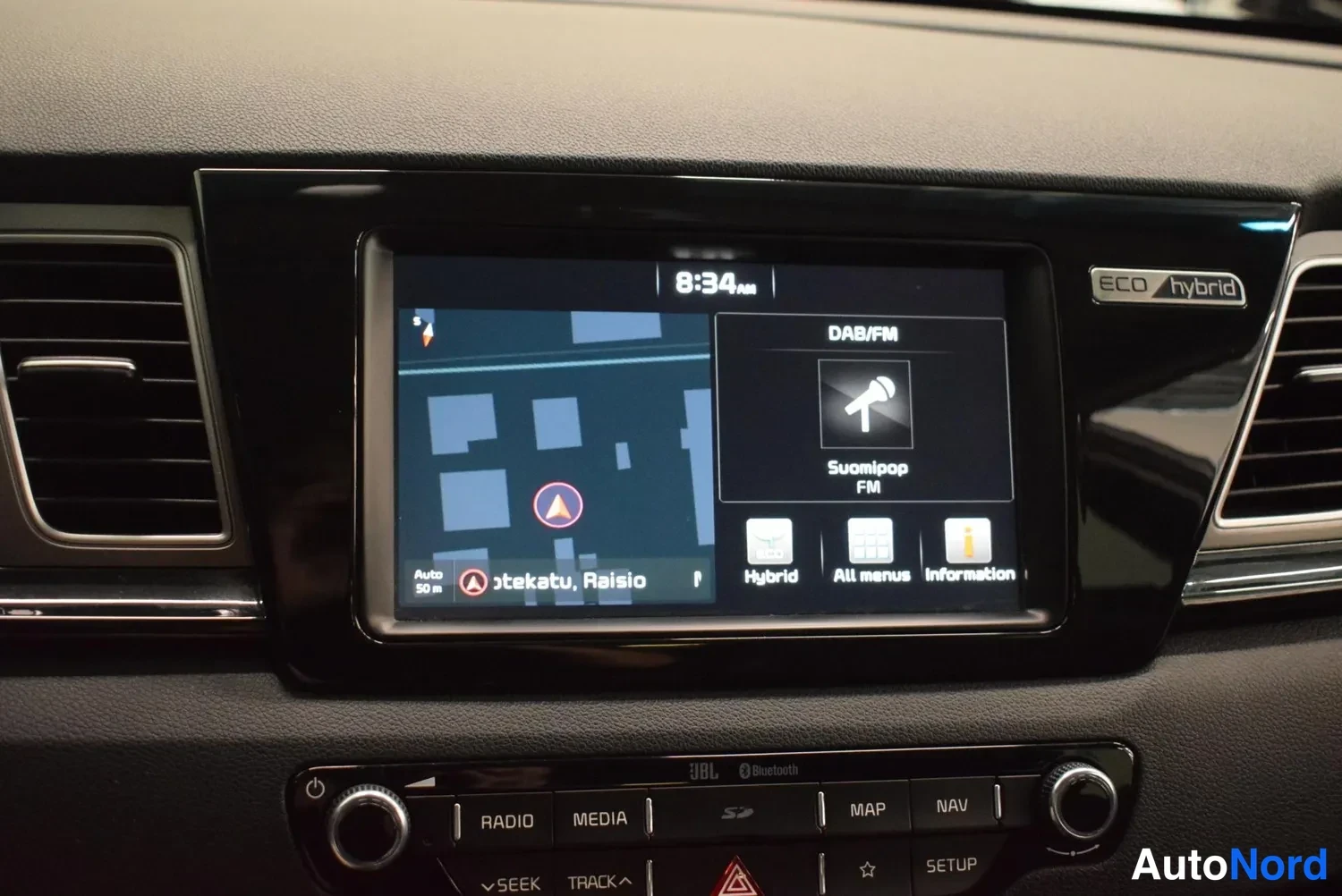 Yksityiskohta: Keskikonsolin kosketusnäyttö näyttää karttaa (otekatu, Raisio) ja DAB/FM-radiota (Suomipop FM); ALC-hybrid-teksti näytön oikealla puolella ja alla RADIO-, MEDIA