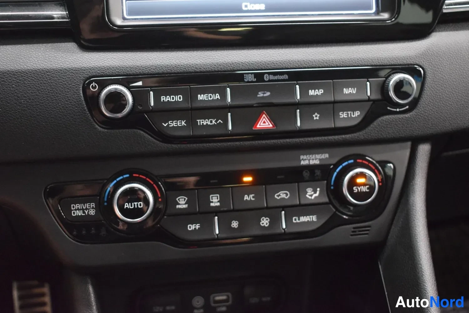 Yksityiskohta: Keskikonsolin äänijärjestelmän ja ilmastoinnin hallintapaneeli. Radiopainikkeet: RADIO, MEDIA, MAP, NAV, SETUP, SEEK, TRACK. Ilmastointipainikkeet: AUTO, A/C, S