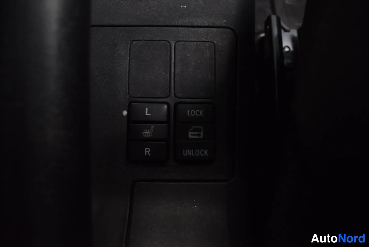 Yksityiskohta: Oven sisäpaneelin sähköikkunan- ja keskuslukituspainikkeet merkinnöillä L, R, LOCK ja UNLOCK, kuva hyvin pimeä.