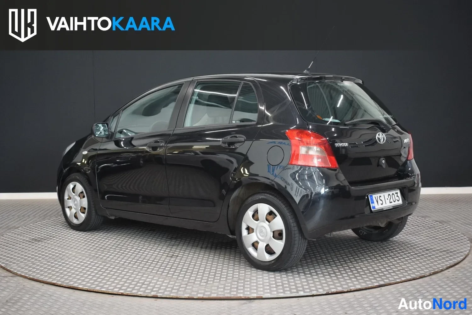 Takaviisto: Musta Toyota Yaris -henkilöauto takaviistosta, rekisterikilpi.