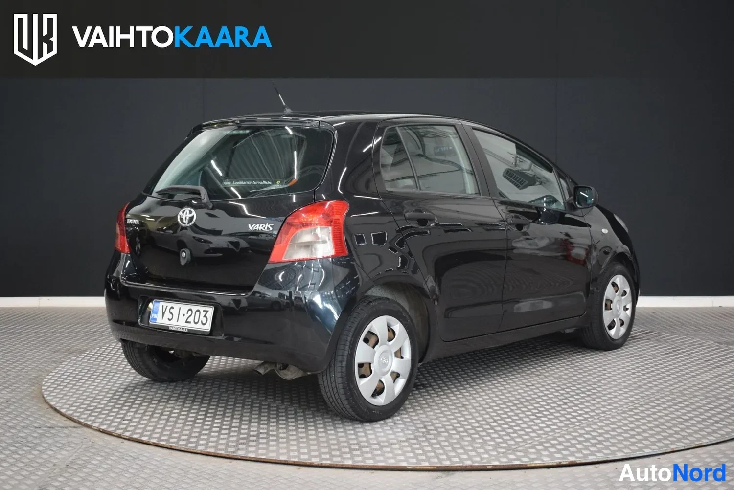 Takaviisto: Musta Toyota Yaris -henkilöauto takaviistosta, rekisterikilpi.