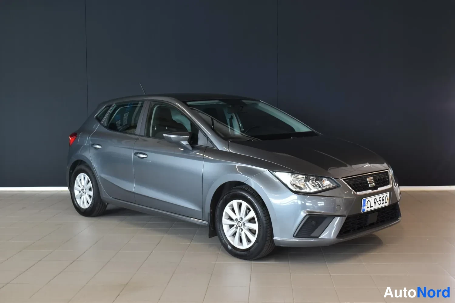 Etuviisto, nokka oikealle: Harmaa Seat Ibiza etukulmasta oikealle kääntyneenä kevythalliin maalattua seinää vasten.