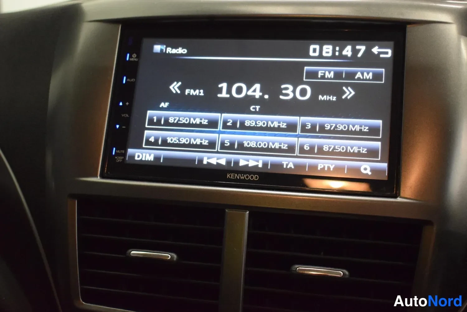 Muu: Lähikuva KENWOOD-radion näytöltä FM1-taajuus 104.30 MHz, esiasetukset listattuna ja aika 08:47.