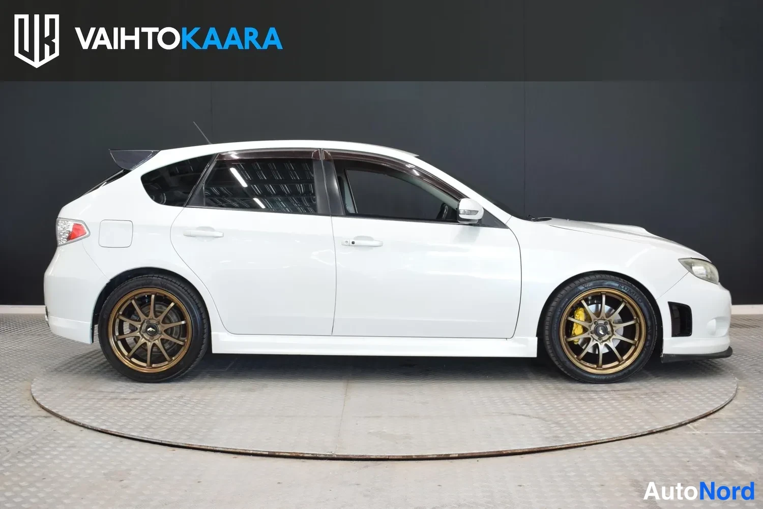 Etuviisto, nokka oikealle: Valkoinen Subaru Impreza WRX -farmari sivulta oikealta katsottuna, pronssiväriset kevytmetallivanteet ja takakannen yllä koroke.