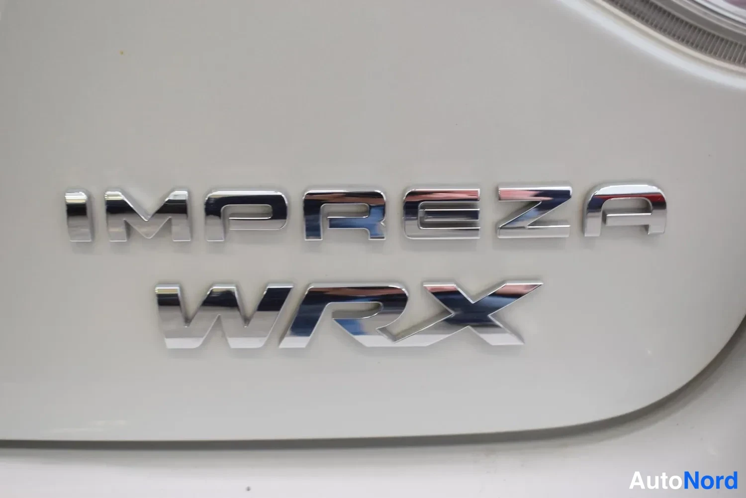 Yksityiskohta: Lähikuva valkoisen auton takaluukun kromikirjaimista IMPREZA WRX.