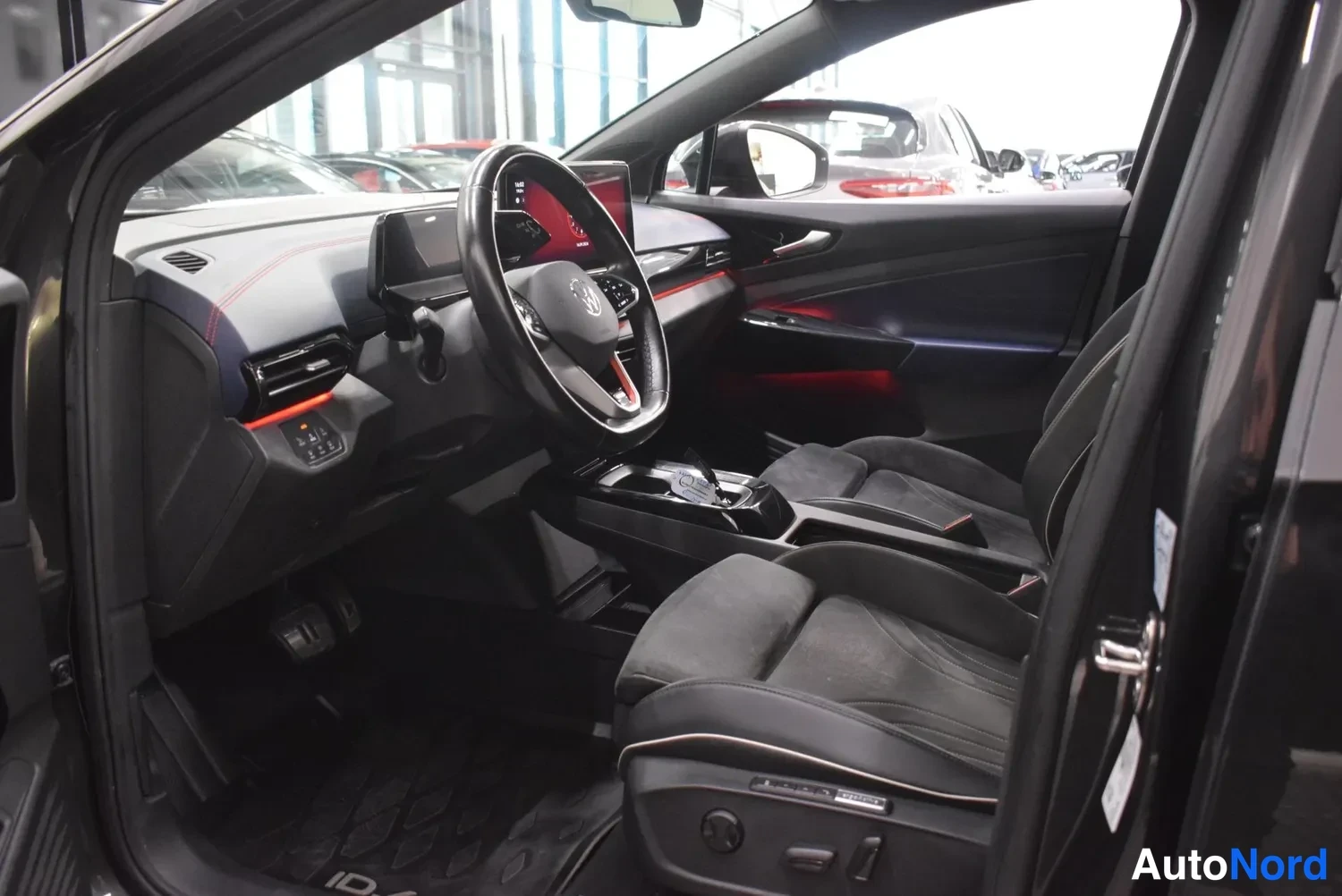 Muu: Mustan Volkswagen ID.4:n etuistuin kilpi: ohjauspyörä, kosketusnäyttö ja tummat urheiluistuimet kuvattuna avatusta etuovesta.