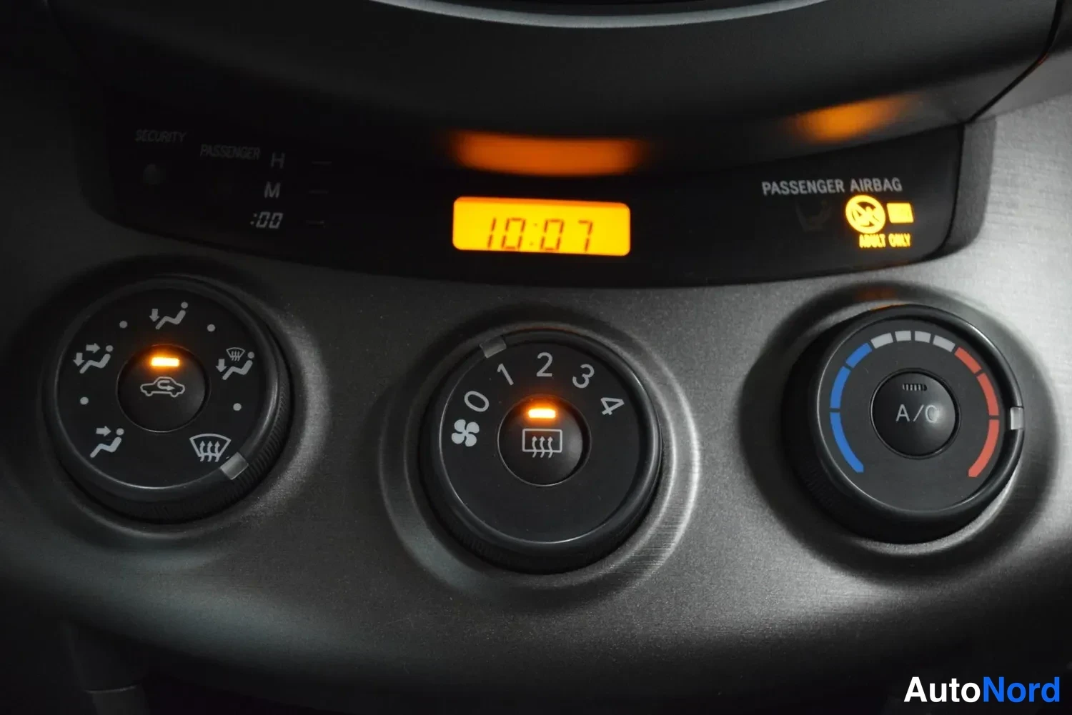 Muu: Ilmastointipaneeli: kierto-, puhallin- (asteikko 0–4) ja lämpötilanuppia, A/C-painike sekä kello 10:07 ja PASSANGER AIRBAG -tekstiä.