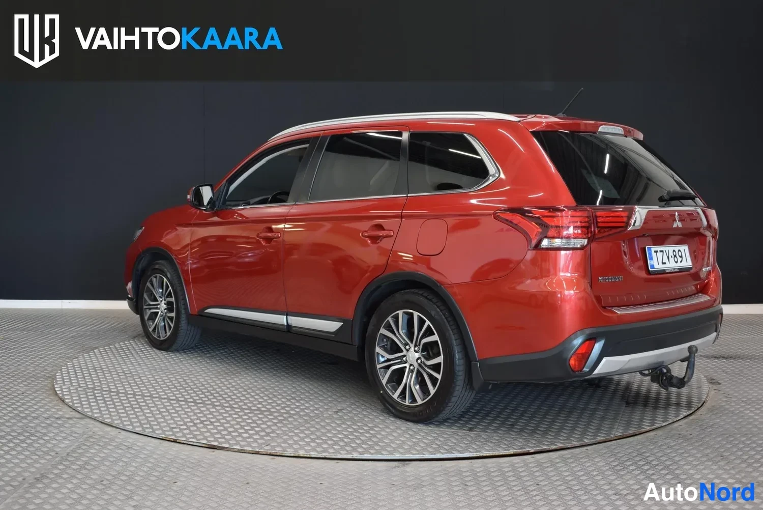 Takaviisto: Punainen Mitsubishi Outlander takaosa oikeasta kulmasta, takavalot ja rekisteri näkyvät, lukkopultti perässä.