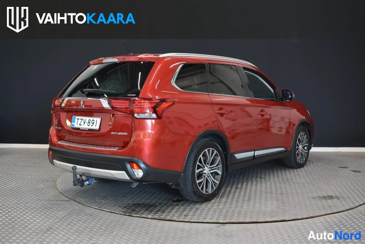 Takaviisto: Punainen Mitsubishi Outlander takaosa vasemmasta kulmasta, takaluukki ja takavalot näkyvät, rekisteri, lukkopultti perässä.