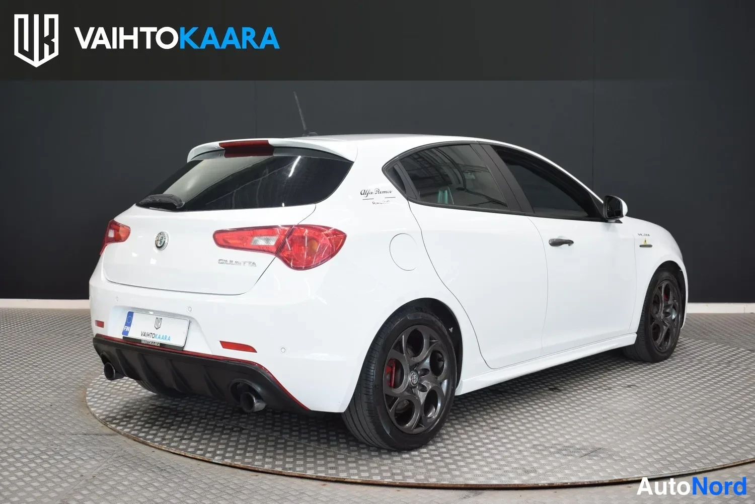 Takaviisto: Valkoinen Alfa Romeo Giulietta -henkilöauto takaa vasemmalta kuvattuna, Giulietta-teksti takaluukussa, kaksiosainen pakoputki ja punaiset jarrusatulat näkyvät.