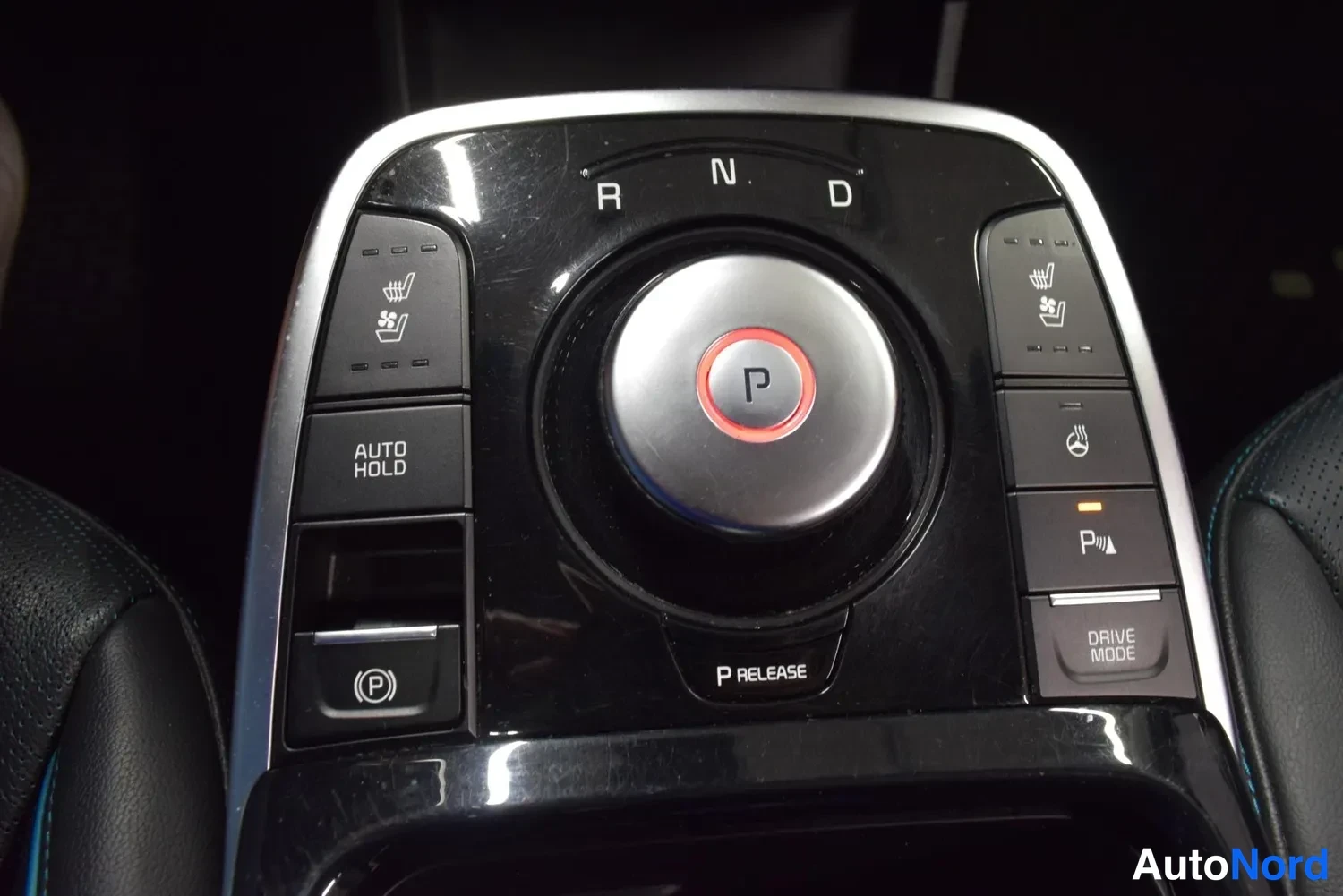 Edestä: Auton keskikonsolin automaattivaihteiston valitsin, jossa näkyvät R, N ja D -merkit, P-nappi, AUTO HOLD ja sähköinen parkkir Jadgnappi sekä lämmitettävien istui