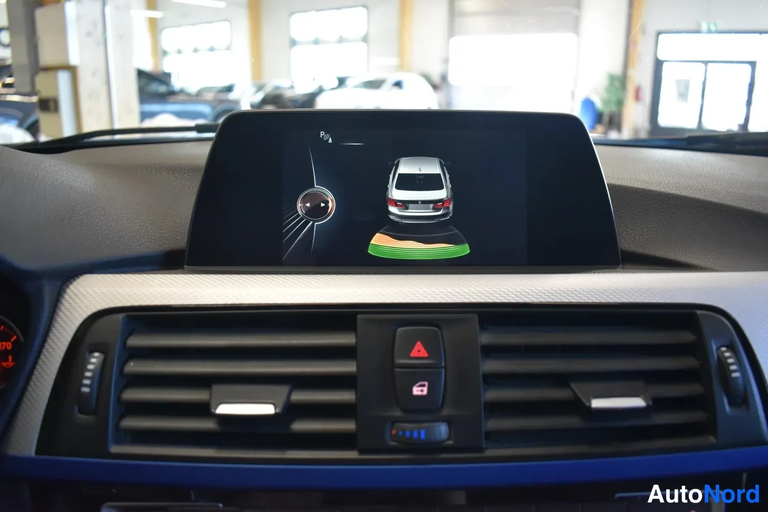Muu: Kojelaudan näyttö näyttää peruutustutkan grafiikan autosta ja etäisyydestä; eteen näkyy ilmastointisuuttimet ja varoituskolmio-painike.