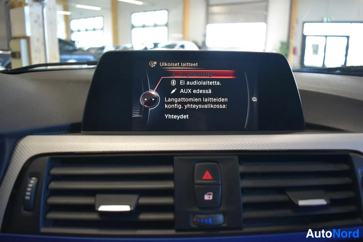 Muu: Auton kojelaudan infotainment-näyttö, jonka valikossa näkyy 'Ulkoiset laitteet' ja Bluetooth-tilatiedot; alla ilmastointisuuttimet.