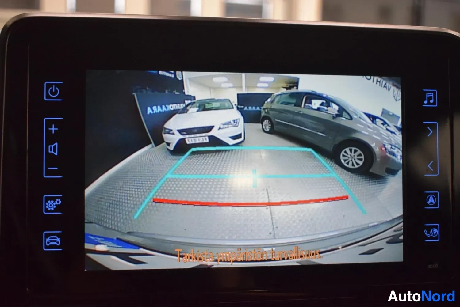 Muu: Infotainment-näyttö näyttää peruutuskameran kuvan pysäköintitiloineen ja varoituksen 'Tarkista ympäristön turvallisuus.'