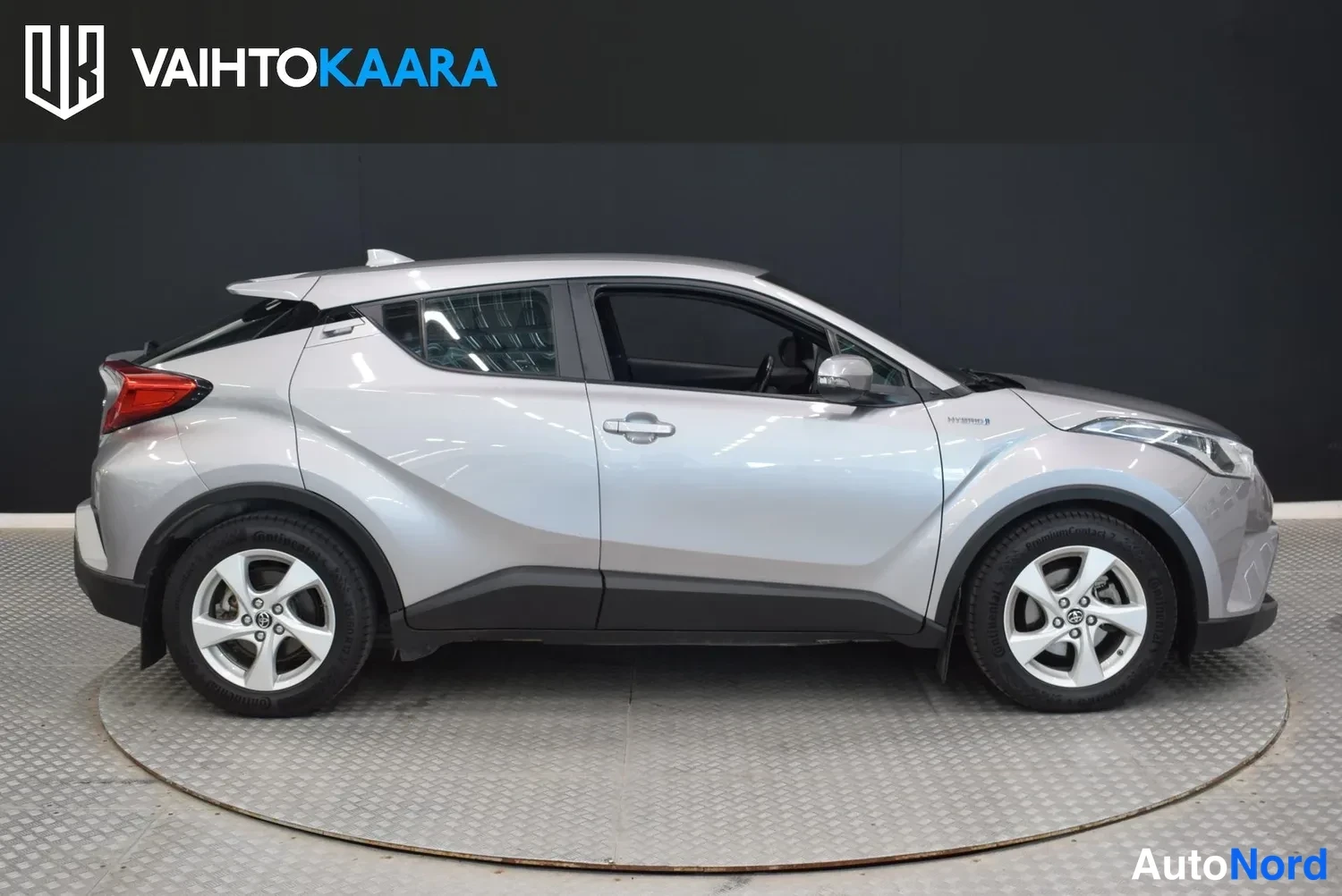 Sivulta: Hopeanharmaa Toyota C-HR -hybridin sivuprofiili studion mustaa taustaa vasten, kylki kokonaan näkyvissä.