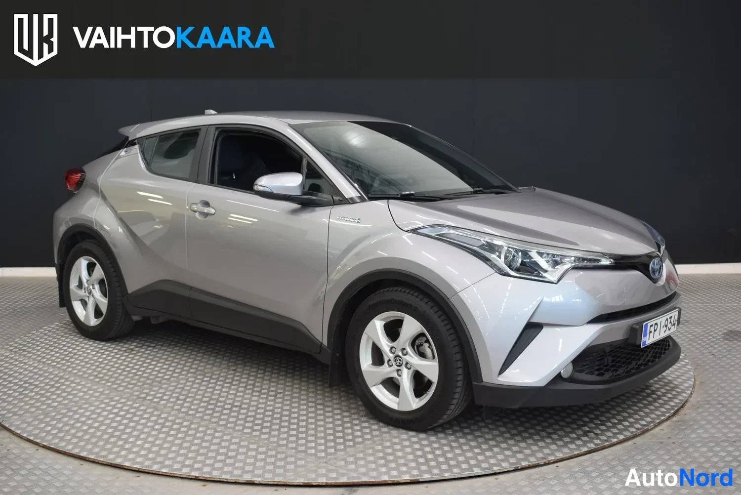 Etuviisto, nokka oikealle: Hopeanharmaa Toyota C-HR etuviistossa oikealta, keulalla rekisteritunnus, studio­tausta.