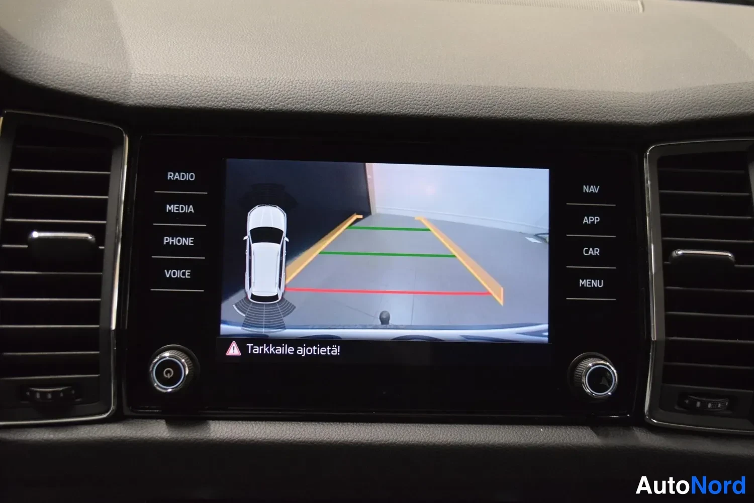 Muu: Infotainment-näyttö näyttää peruutuskameran kuvan pysäköintilinjoilla ja varoituksen Tarkkaile ajotietä!.