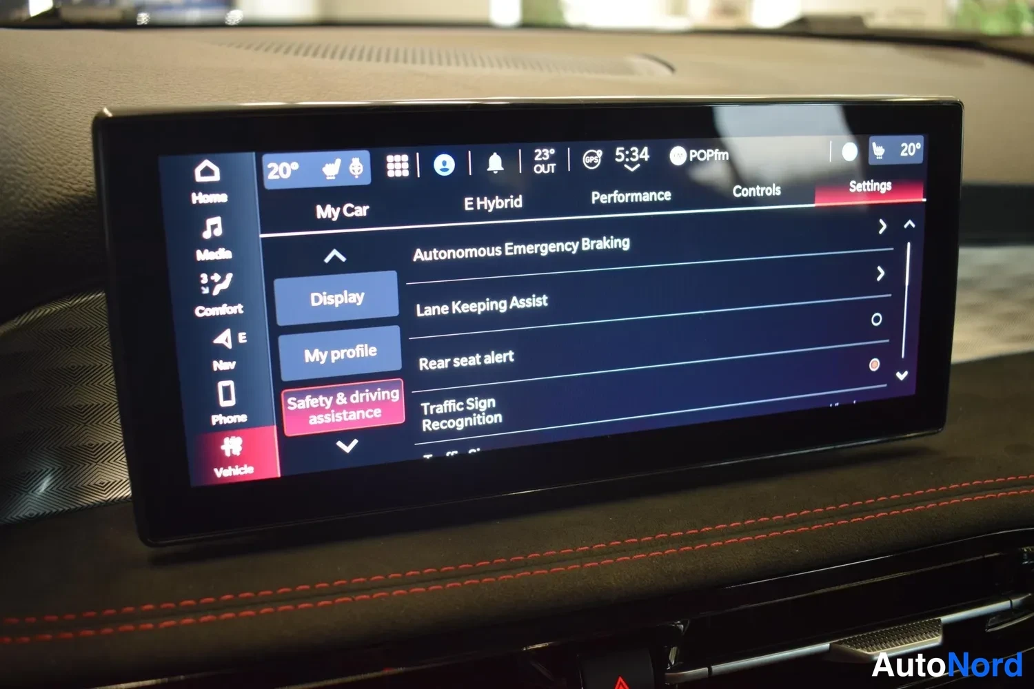 Yksityiskohta: Kojelaudan infotainment-näyttö, jossa on avoin Settings-valikko ja Safety & driving assistance -osio muun muassa Autonomous Emergency Braking- ja Lane Keeping A