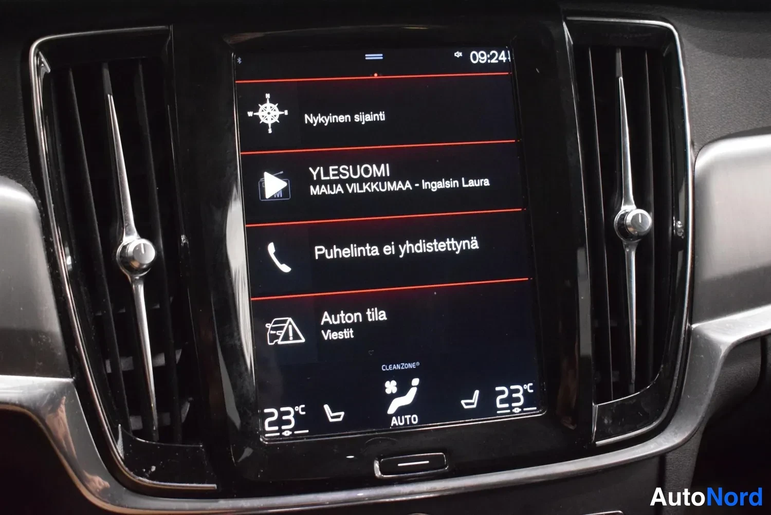 Muu: Kojetaulun keskellä oleva pystysuora infotainment-näyttö valikossa, jossa kohteet Nykyinen sijainti, radio YLESUOMI, ilmoitus Puhelinta ei yhdistetty ja Auton t