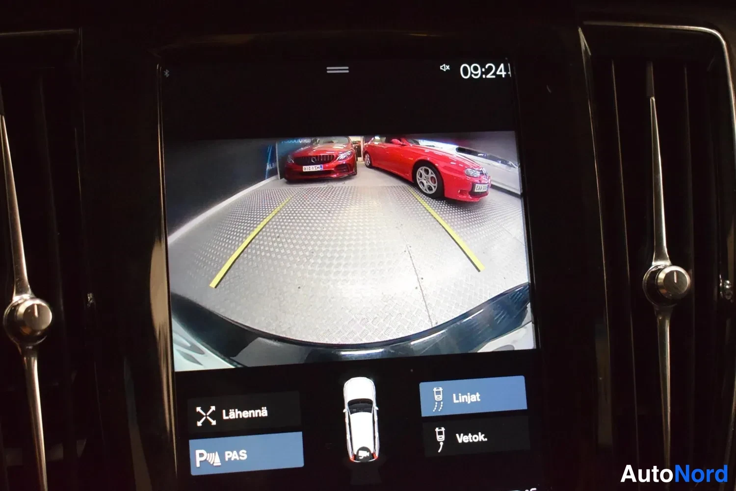 Muu: Infotainment-näyttö näyttää takakameran kuvan parkkihallista, jossa punaisia autoja vieressä; alareunassa painikkeet Lähennä, PAS, Linjat ja Vetok.