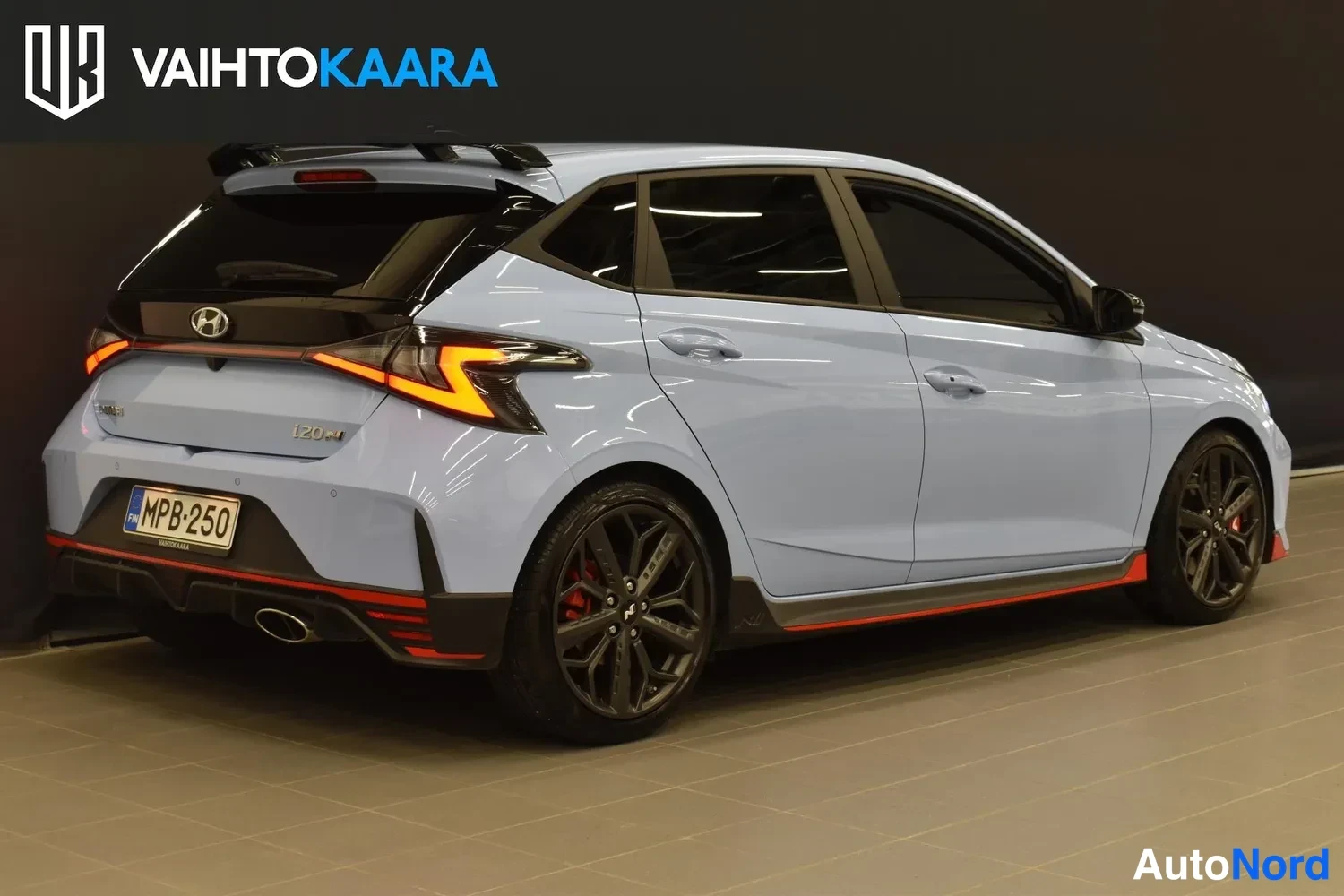 Takaviisto: Vaaleansininen Hyundai-liftback takaviistosta vasemmalta, punaiset jarrusatulat ja tummat kevytmetallivanteet näkyvissä.