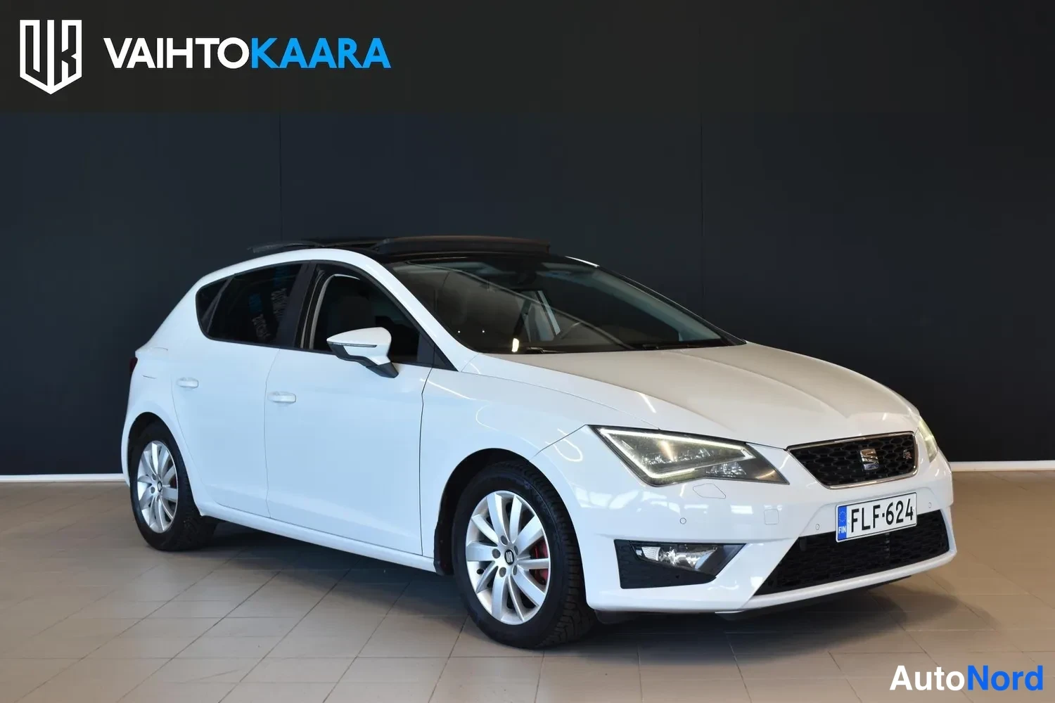 Etuviisto, nokka oikealle: Auton keula viistosti oikealta: valkoinen Seat Leon, kylki ja etusäleikkö näkyvissä, rekisterikilpi, kattoluukku.