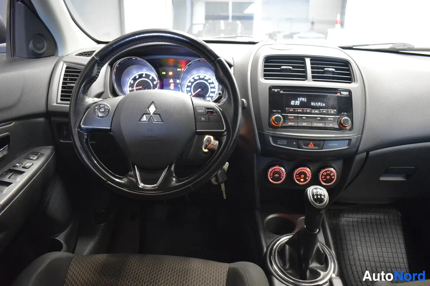 Muu: ohjaamo suoraan edestä: Mitsubishi-ohjauspyörä, mittarit, radio näytöllä FM1 10:33 MitMix, lämmitysvalitsimet ja manuaalivaihteiston keila 1–5 ja R