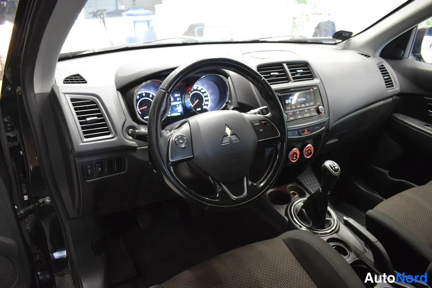 Muu: Auton ohjaamo näkyy kuljettajan puolelta: Mitsubishi-merkillä varustettu ohjauspyörä, analogiset mittarit, keskikonsolissa radio ja manuaalivaihteiston vaihdevi