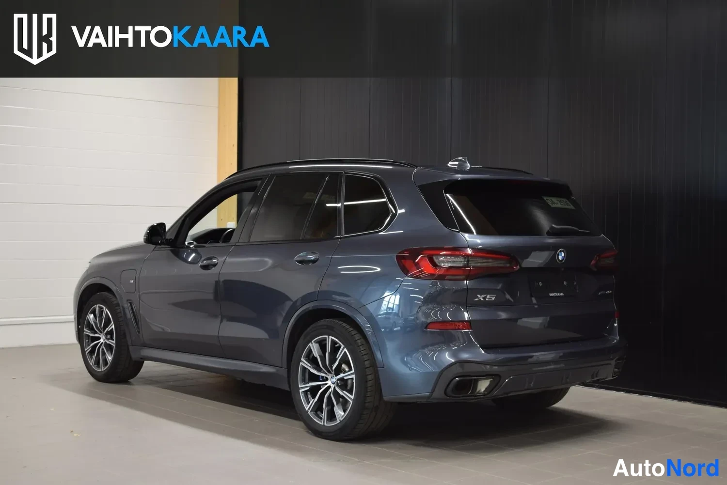 Takaviisto: Sinisenharmaa BMW X5 takanurkkakuva vasemmalta sisätiloissa, X5-merkintä peräovessa.