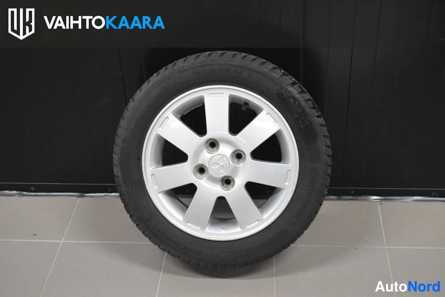 Yksityiskohta: Hopeanvärinen Mitsubishi-vakiovanne renkaalla ContiWinterContact TS 850 talvirenkaana mustaa seinää vasten.
