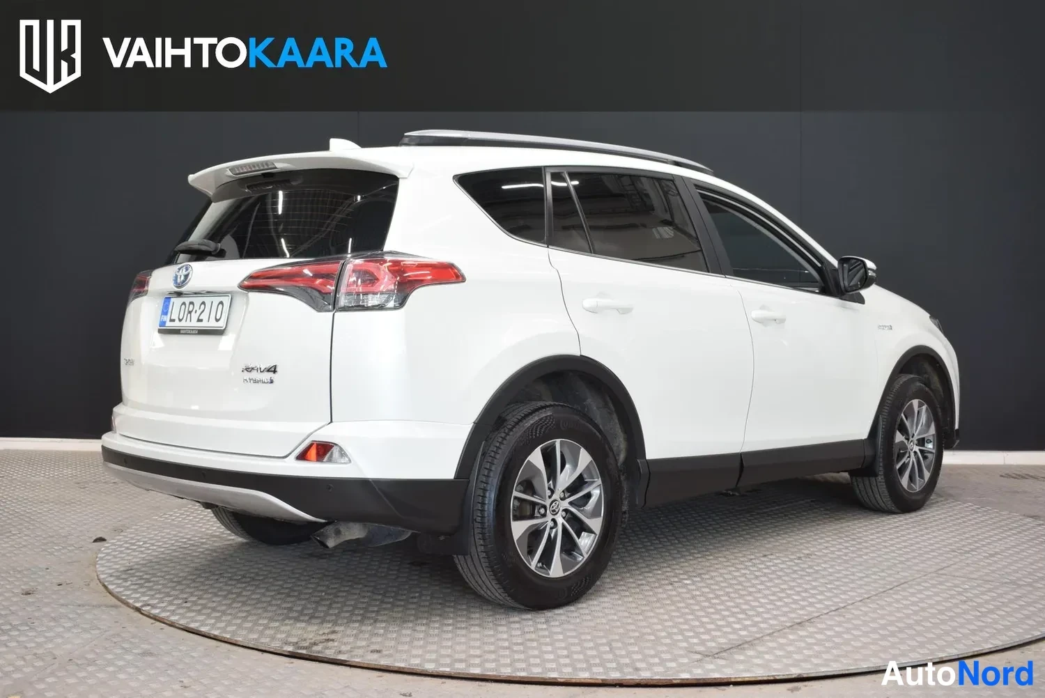 Takaviisto: Valkoinen Toyota RAV4 takakulmasta vasemmalta kuvattuna studiokuvassa, rekisterikilpi näkyvissä.