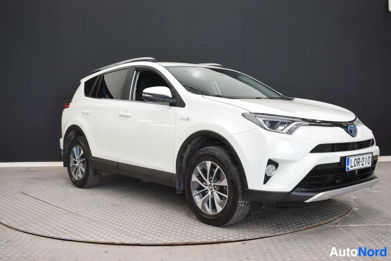 Etuviisto, nokka oikealle: Valkoisen Toyota RAV4:n etukulmakuva oikealta etualalla, etusäleikkö ja rekisterikilpi näkyvät.