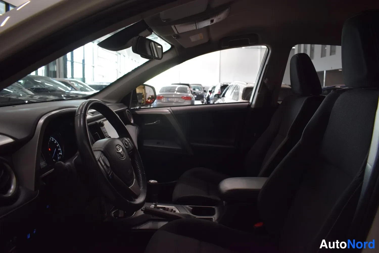 Muu: Toyota RAV4:n ohjaamo etuistuimilta taaksepäin kuvattuna, ratin osa ja kaksi etuistuinta näkyvät hämärässä.