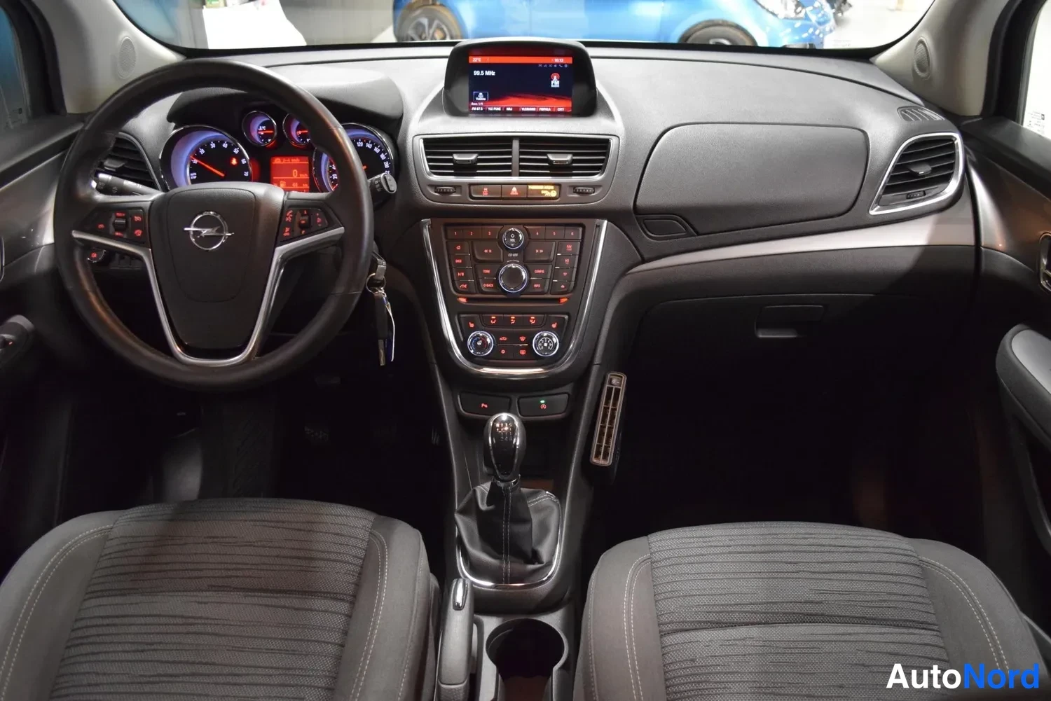 Sivulta: Kojelauta ja etuistuimet eteenpäin: Opel-merkitty ohjauspyörä, Analogiset mittarit, keskikonsolissa näyttö, manuaalivaihteen keila ja jarrukahva.