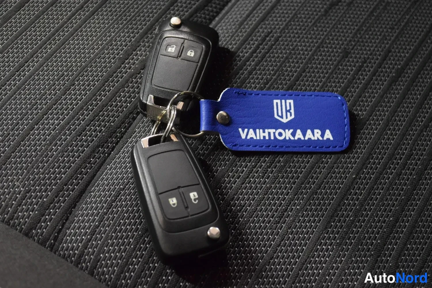 Muu: Kaksi mustaa kauko-ohjainta ja sininen Vaihtokaara-avainnauha kangaspinnalla.