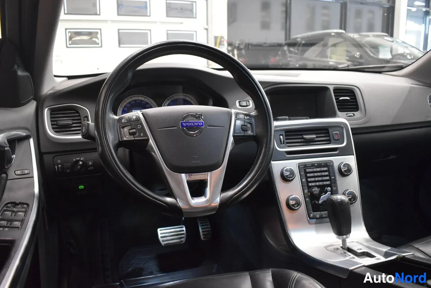 Edestä: Auton sisätilat: Volvo-ohjauspyörä, siniset mittarit, automaattivaihteiston valitsin ja keskikonsoli.