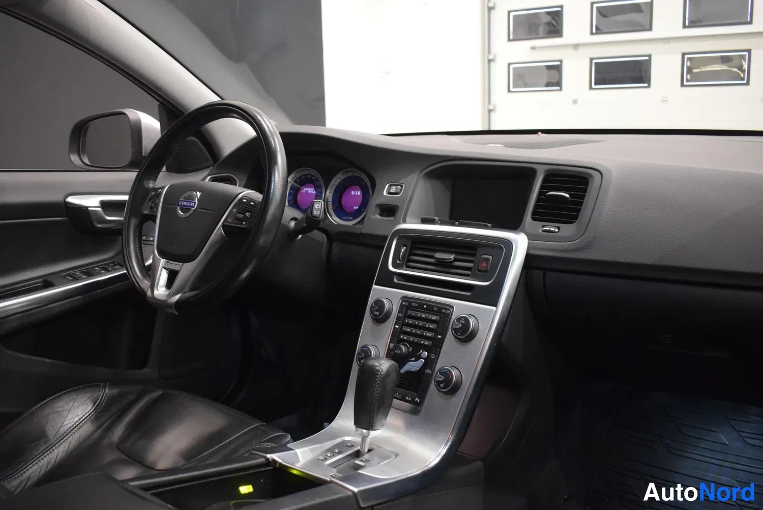 Muu: Volvo V60:n ohjaamo kuvattu kuljettajan puolelta: musta nahkainen ohjauspyörä, mittaristo ja keskikonsoli, automaattivaihteen valitsin ja tummat verhoilut.