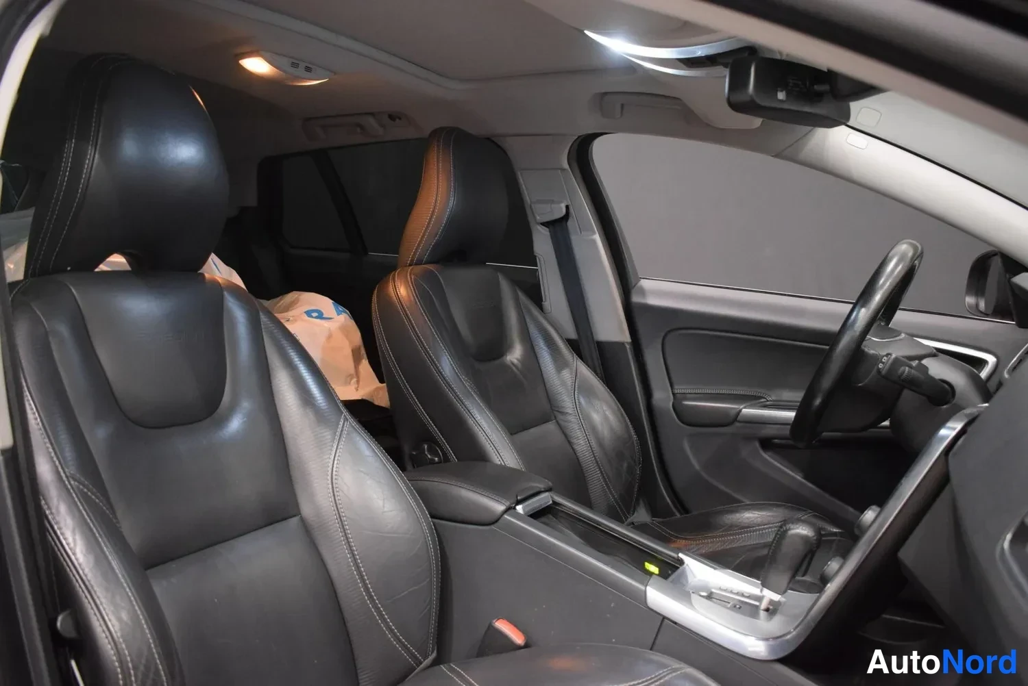 Muu: Volvo V60:n etuschat istuimet mustaa nahkaa etupenkillä, kaksiosainen selkänoja ja keskiarkku näkyvät takaa-ajettavasta istuimesta; mittarit ja ohjauspyörä osit
